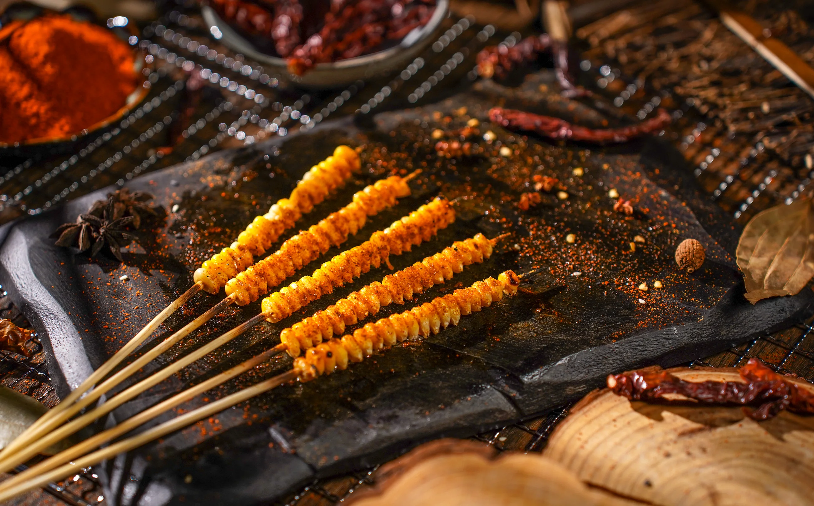 Grilled corn skewers dusted with chilli on a slate