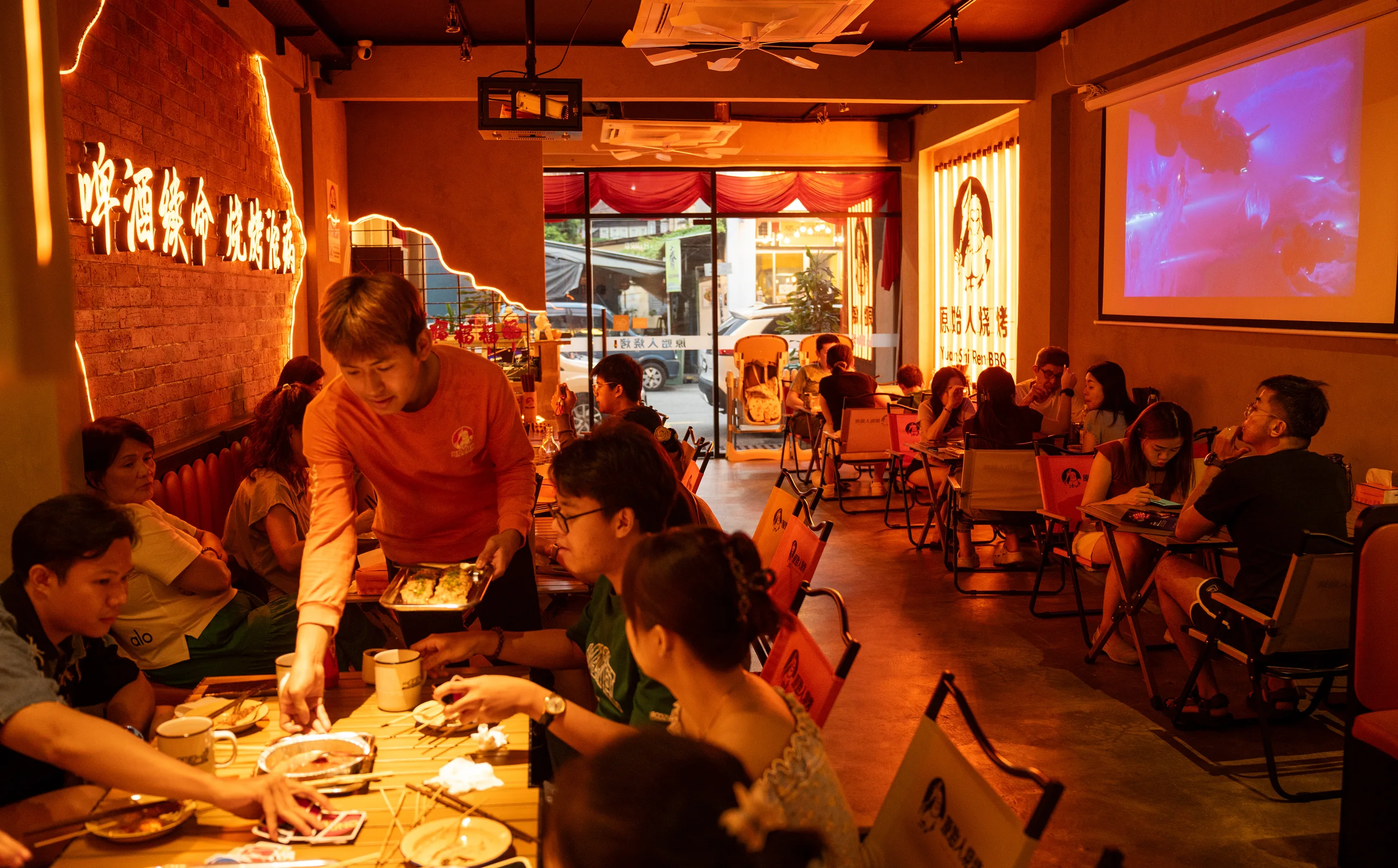 Staff serving skewers to a full table under the orange lights at Yuan Shi Ren BBQ George Town