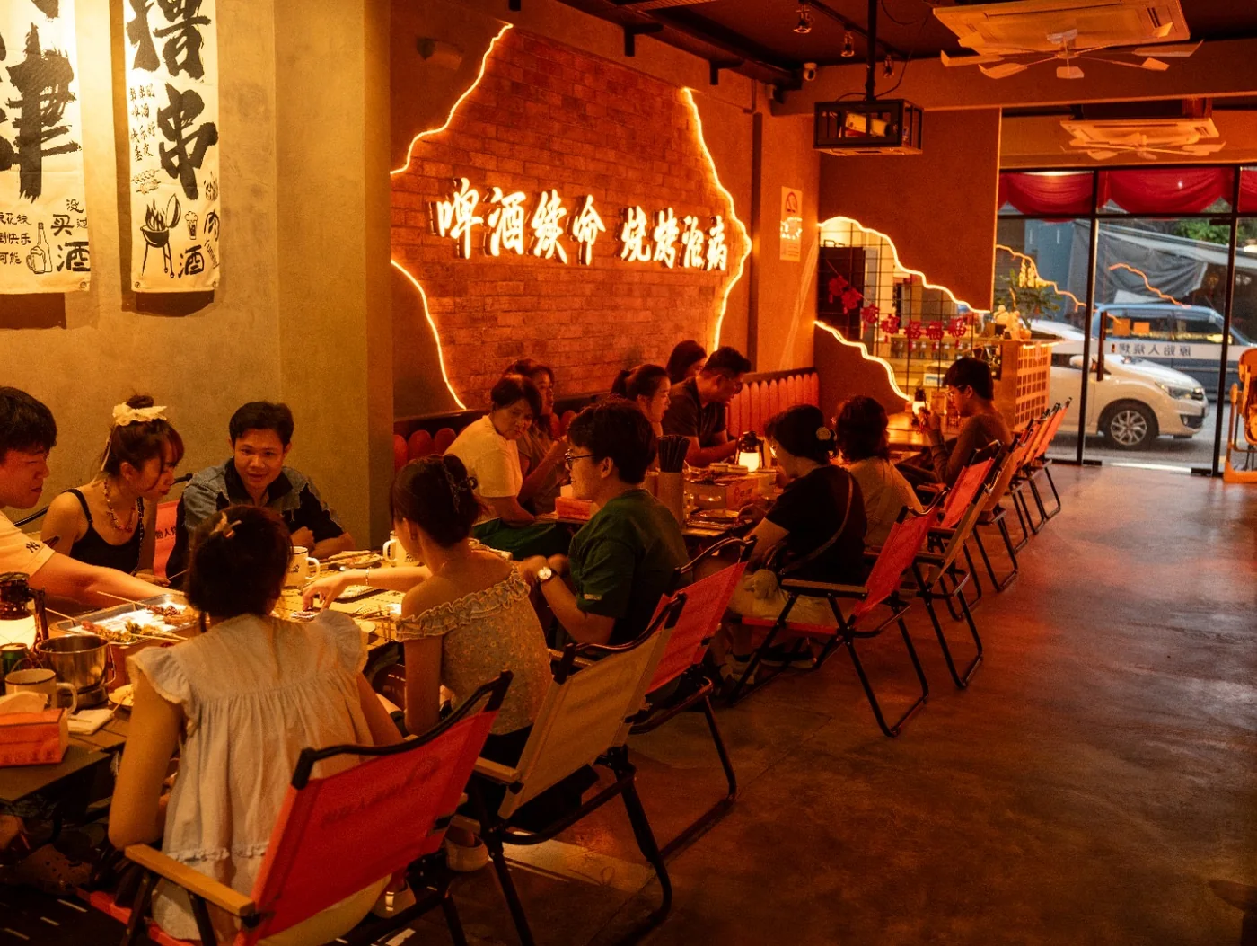 Guests at camping tables under the neon slogan wall in George Town
