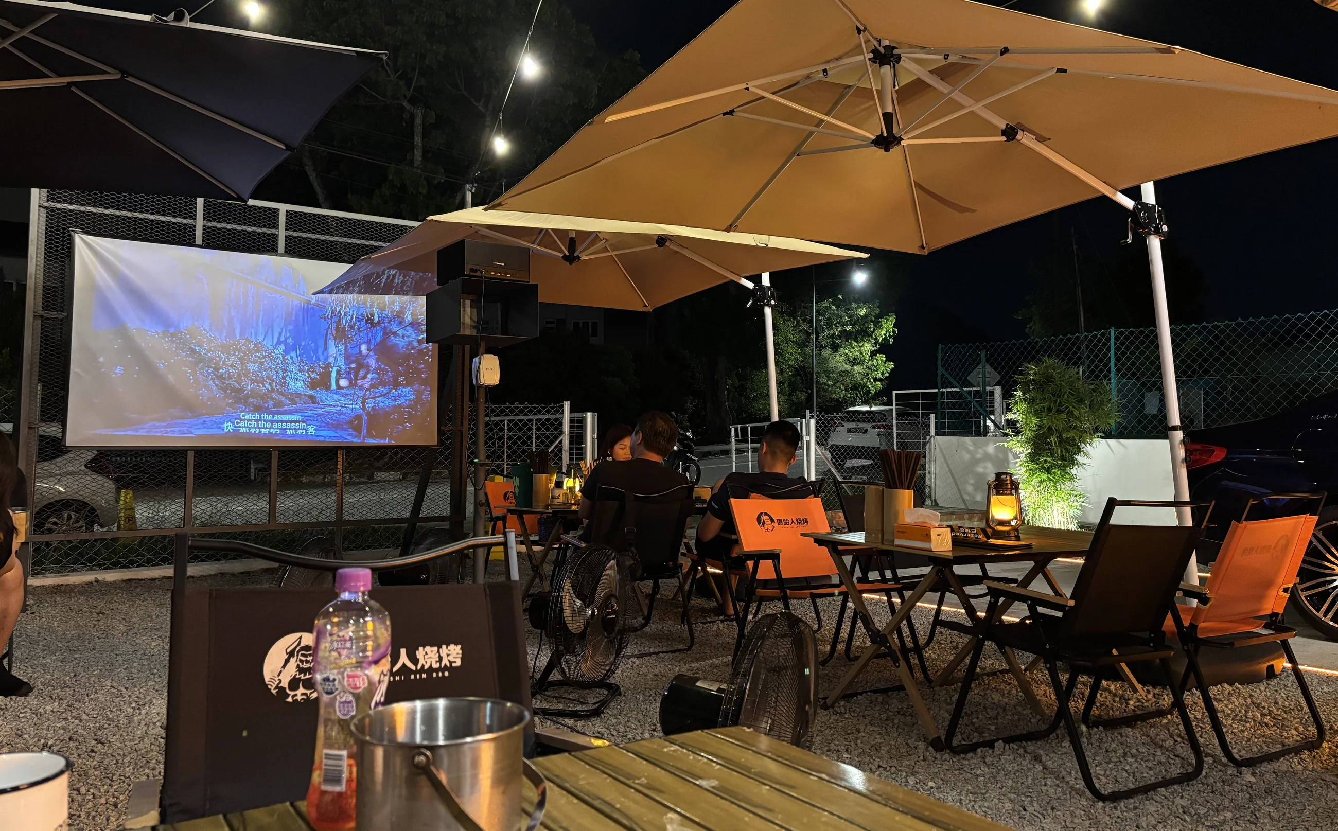 Open-air garden seating with umbrellas and an outdoor screen at the Tanjung Bungah outlet